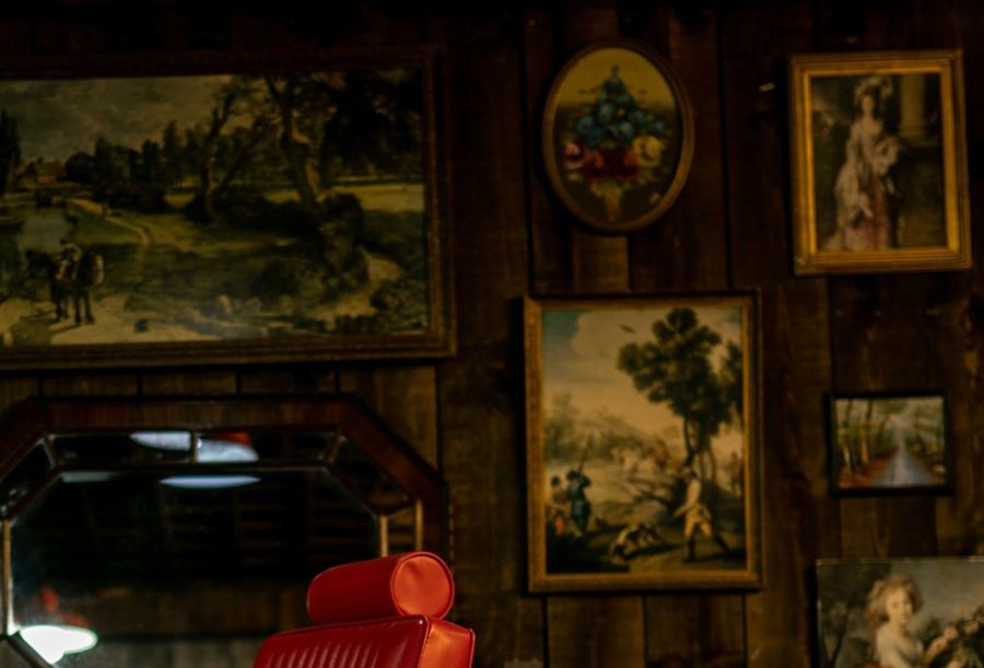The wall of framed pictures hung above the red chair, close in