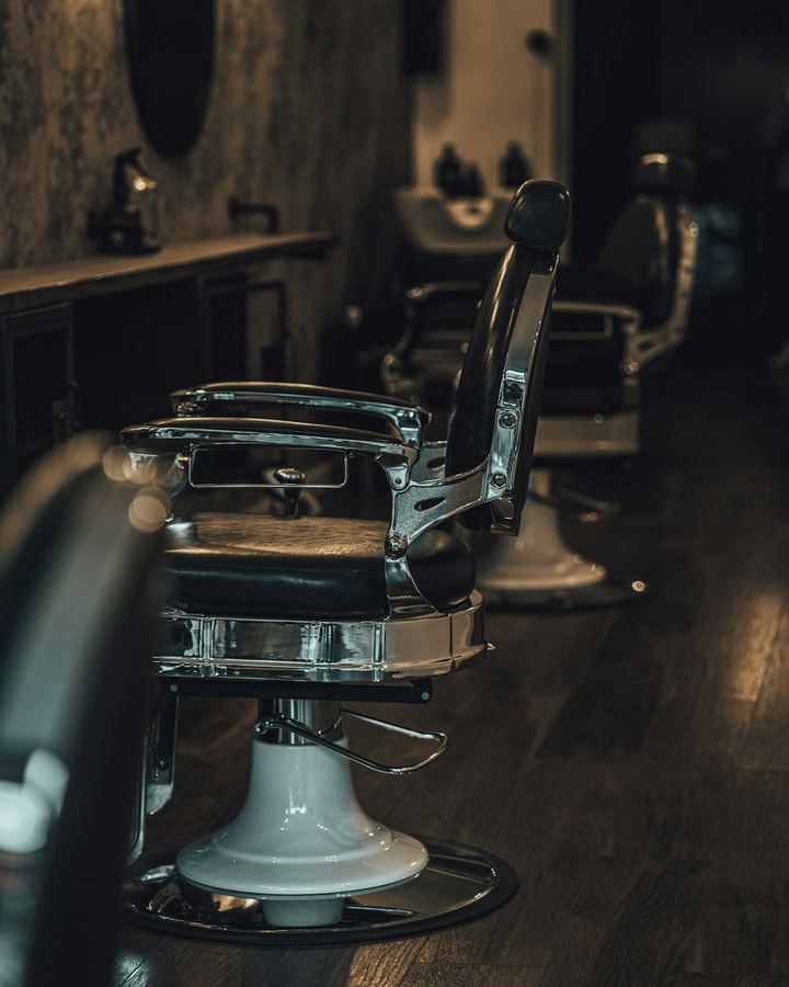 A chrome barber's chair standing alone on the shop floor, the room dark behind it