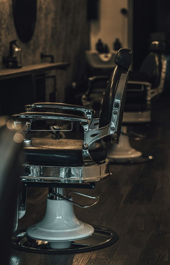 A chrome barber's chair photographed head on, the shop dark around it